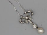 une photo d'un pendentif en forme de nœud, orné d'une perle et d'un diamant, monté sur une chaîne