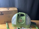 une photo d'un aspirateur vert et blanc posé sur une table, à côté d'une boîte