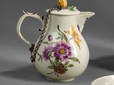 a white pitcher with flowers on it next to a bowl