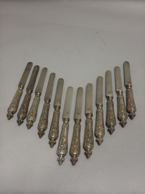 six couteaux en métal argenté sont alignés en rang sur une surface blanche