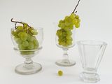 three glass vases with grapes in them on a white surface
