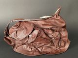brown leather purse with ruffles on top of it sitting on a table