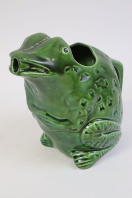 un vase en forme de grenouille verte posé sur une surface blanche