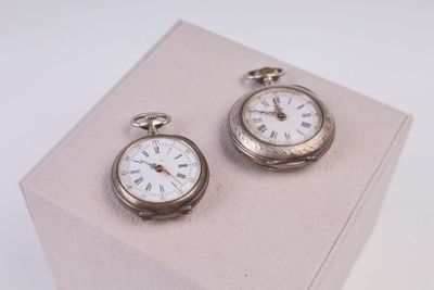 deux montres de poche en argent posées sur un présentoir rose
