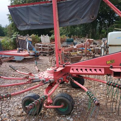 une image représentant un tracteur rouge équipé d'un râteau à l'arrière
