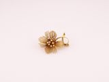 un gros plan d'une bague en forme de fleur dorée posée sur une surface blanche
