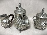 trois théières en argent posées sur une surface blanche