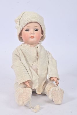a baby doll sitting on the ground wearing a sweater and hat