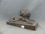 statue d'un lion posée sur un socle en bois, sur fond gris