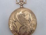 a gold pocket watch with a bird on it