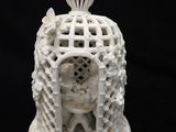 une figurine blanche représentant un oiseau dans une cage, sur fond noir