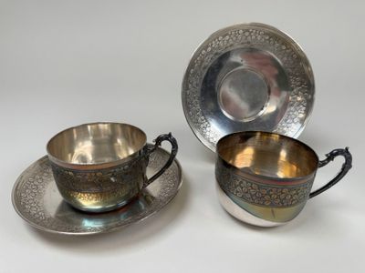 two silver plated cups and saucers on a white surface