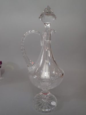 un pichet en verre transparent posé sur une table à côté d'un vase violet