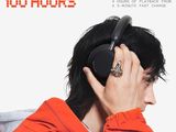 a man in an orange jacket holding a pair of headphones to his ear