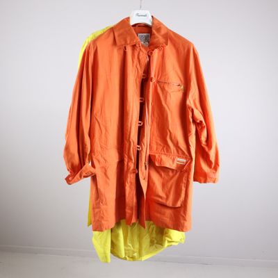 an orange jacket hanging on a hanger in front of a white wall