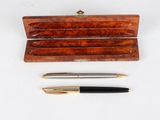 deux stylos et un étui en bois posés sur une surface blanche