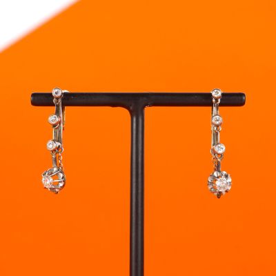 silver plated earrings on a black stand against an orange background