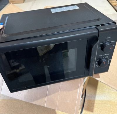 un micro-ondes noir posé sur un carton posé à même le sol