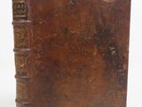 an old brown book sitting on top of a table next to a white wall