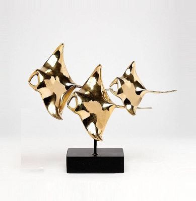 brass sculpture of three fish on a black base on a white background