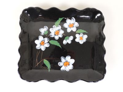 une assiette noire sur laquelle sont peintes des fleurs blanches et orange