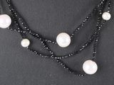 a close up of a black and white necklace with pearls