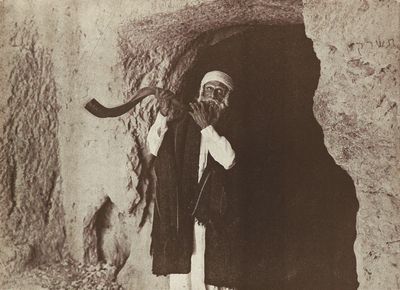 a black and white photo of an old man holding a pipe