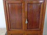 une armoire en bois à deux portes, sur laquelle est posé un vase avec des fleurs