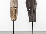 deux masques en bois posés sur des socles dans une pièce aux murs blancs