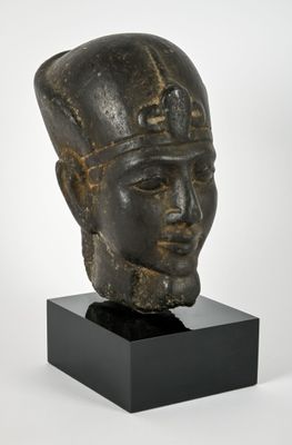 une tête d'homme en bronze coiffée d'un chapeau, posée sur un socle noir