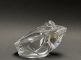a glass frog figurine sitting on a black surface