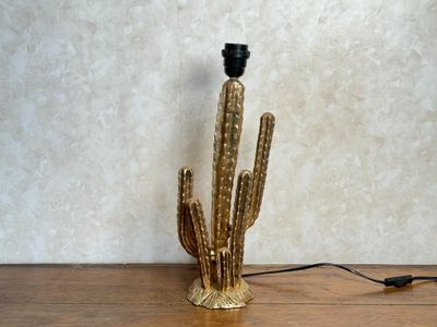 une lampe en forme de cactus dorée posée sur une table en bois, avec un cordon noir