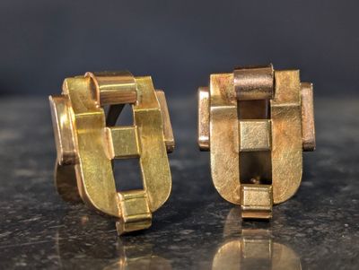 pair of gold tone cufflinks on a shiny surface with a black background