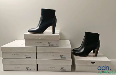 deux paires de bottes noires à talons hauts posées sur une pile de cartons blancs