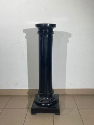 black marble pedestal on tiled floor with white wall in background