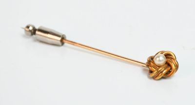 une broche en or sertie d'une perle, posée sur un fond blanc