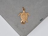 gold plated sea turtle charm on a grey surface