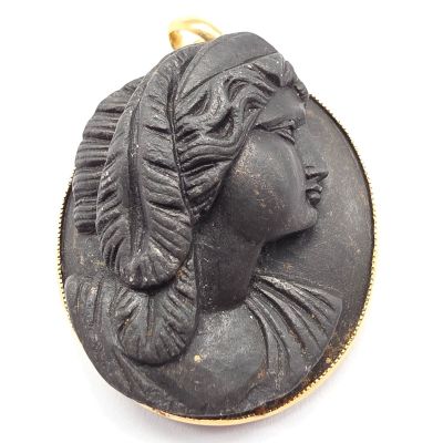 un gros plan sur un pendentif noir et doré représentant le visage d'une femme