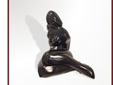 une statue noire représentant une femme assise sur une surface blanche