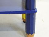 a blue table with two yellow legs and a blue shelf