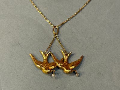 two birds that are hanging from a gold necklace