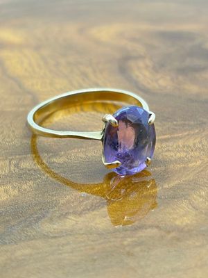 bague en or jaune sertie d'une pierre violette, posée sur un support en bois