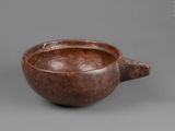 an old wooden bowl with a handle on a gray surface