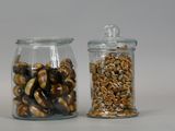 two glass jars with nuts in them on a white surface