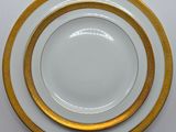 trois assiettes blanches et dorées, bordées d'or, posées sur une table blanche