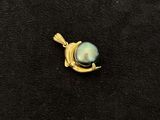 a close up of a gold pendant with a pearl on it