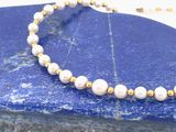 collier composé de perles et de perles dorées, posé sur une plaque de marbre bleu