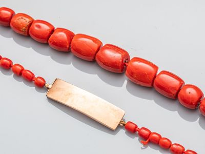 deux perles de corail rouge et une barre dorée sur un fond blanc
