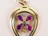 a close up of a gold pendant with a purple flower on it