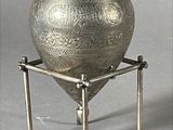 a silver vase that is on a stand on a gray background